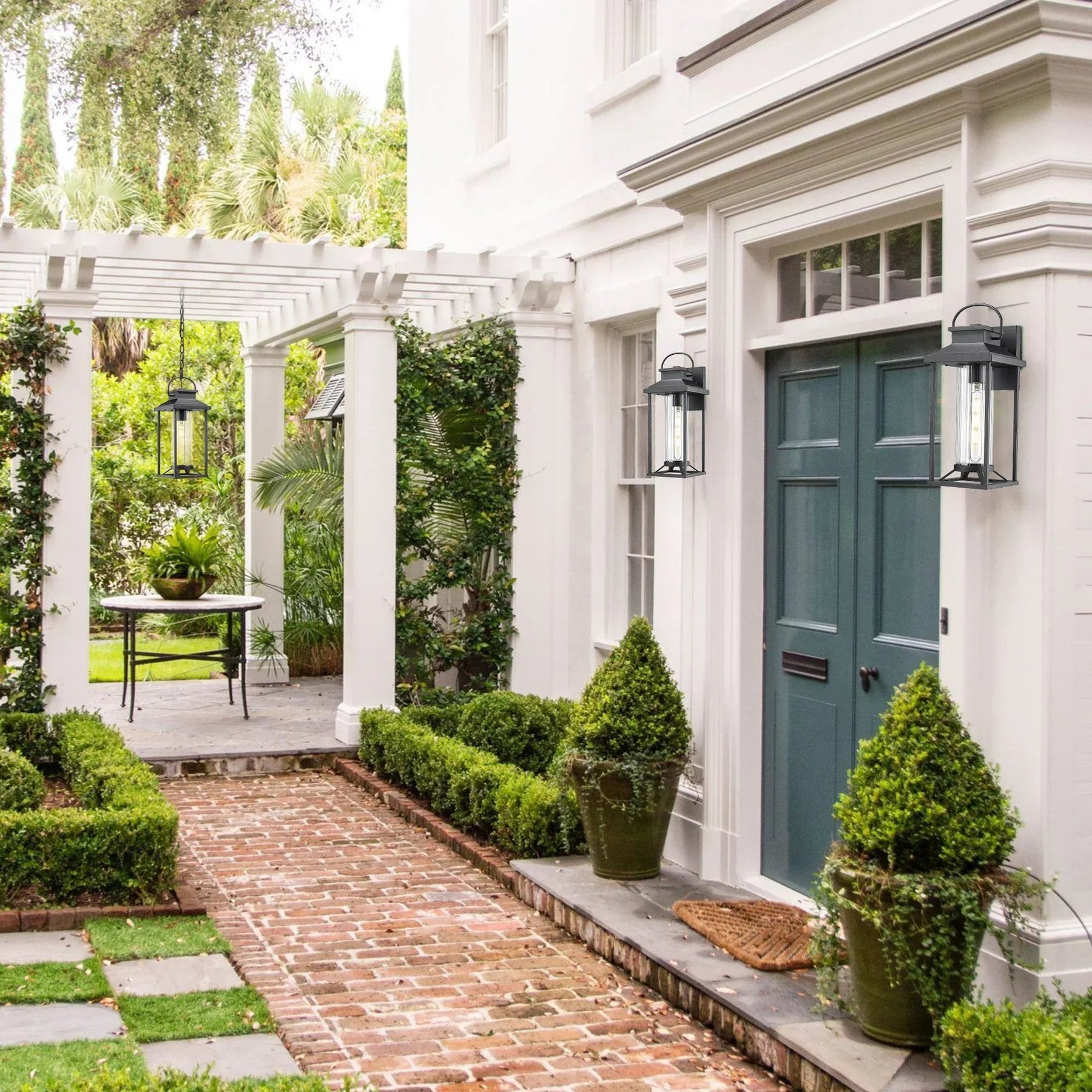 Black exterior lighting fixtures on white house with green door, brick path, and garden