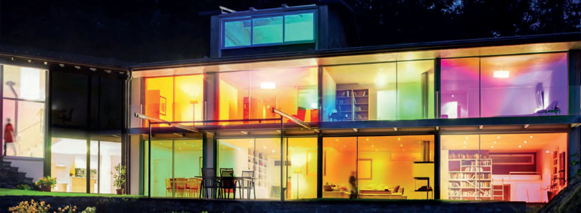 Modern house with large glass windows displaying colorful dimmable LED lights at night