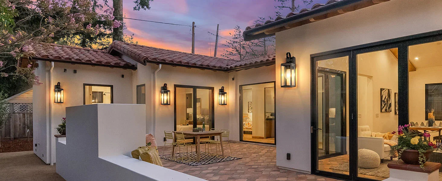 Modern outdoor lighting fixtures on a patio of a white stucco house at sunset.