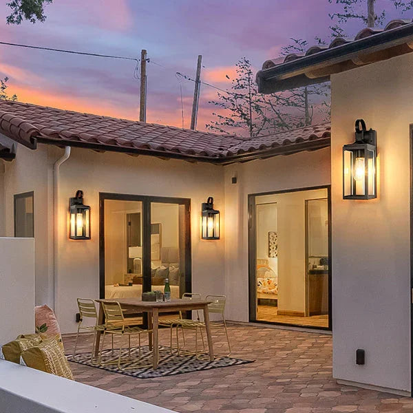 Modern outdoor lighting fixtures on a patio of a white stucco house at sunset.