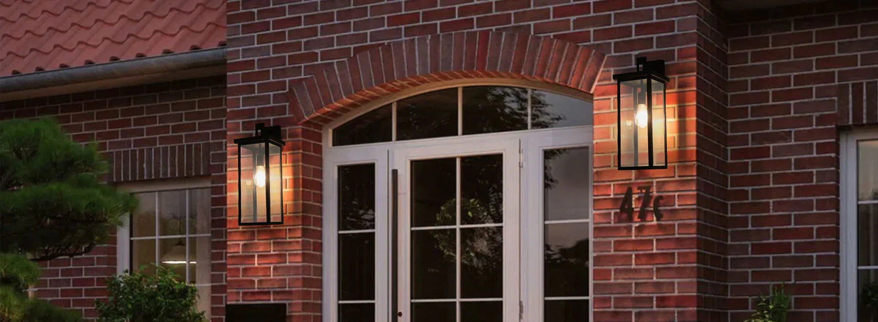 Classic black outdoor wall lights on red brick house next to white double doors