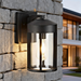 Black outdoor wall light fixture on a stone wall with a modern house in the background